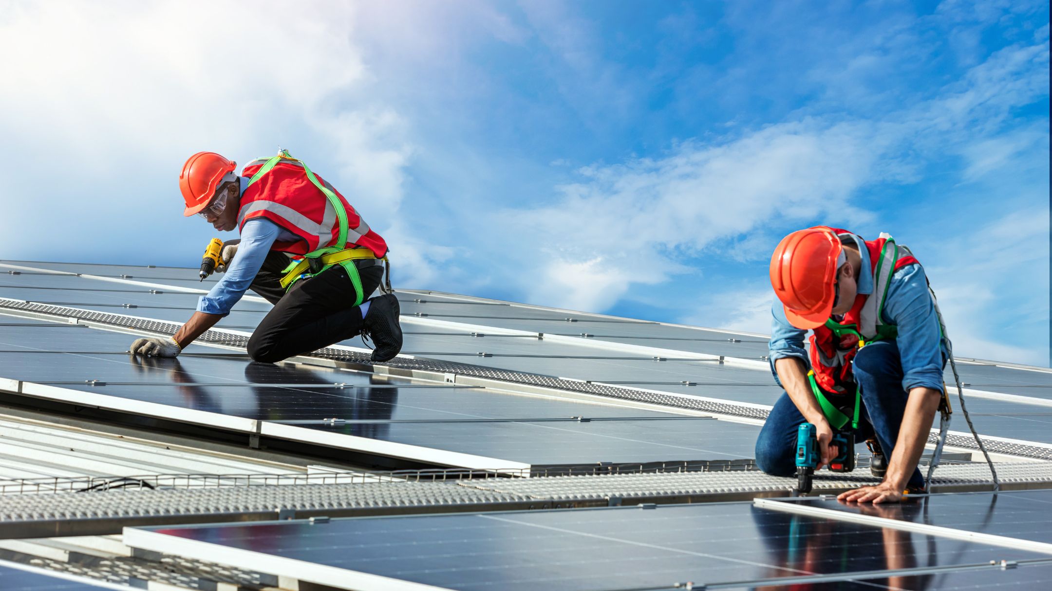 Dos instaladores con casco montando paneles solares en un techo